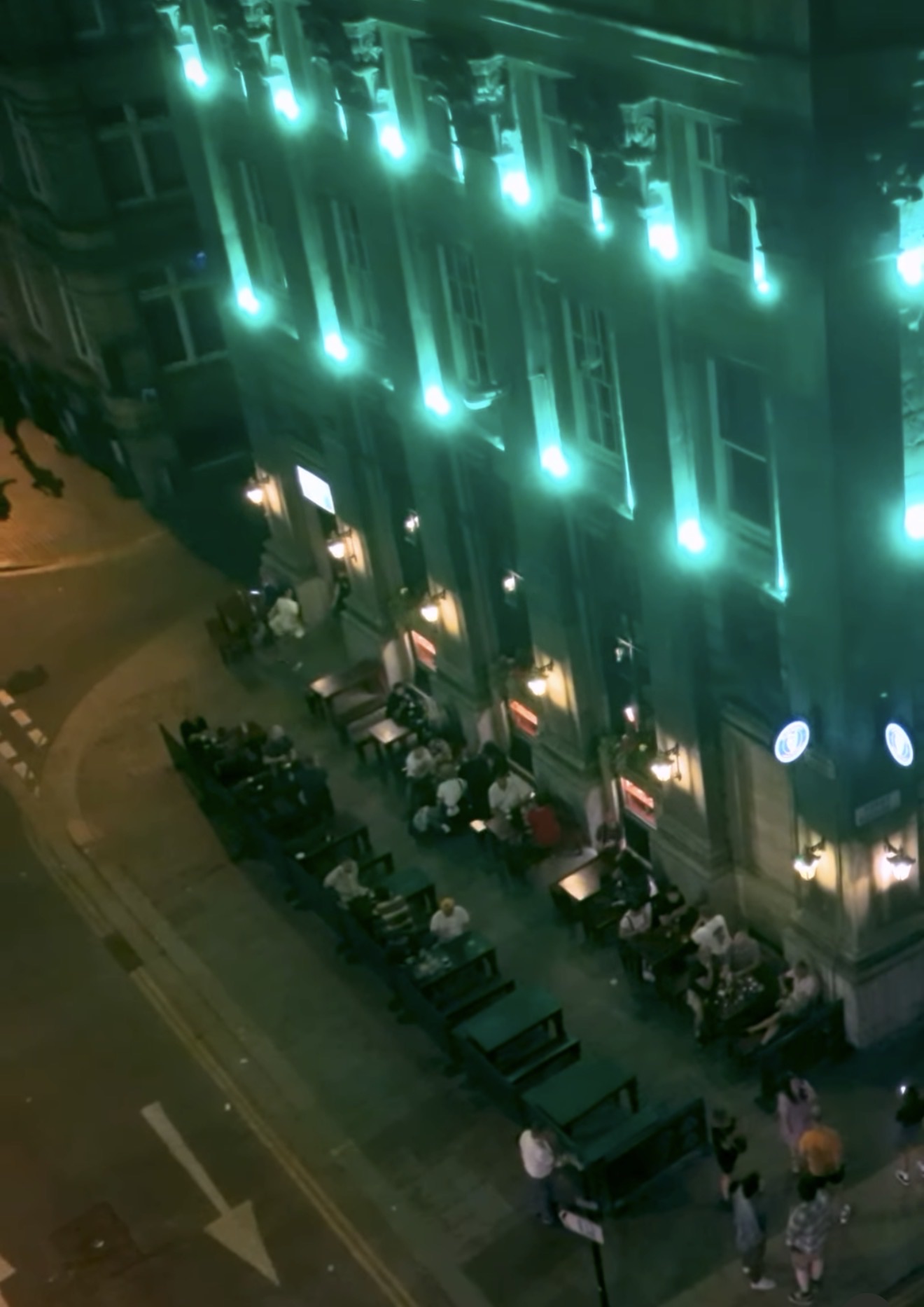 The McSwiggin’s facade lit green at night with a full pavement terrace